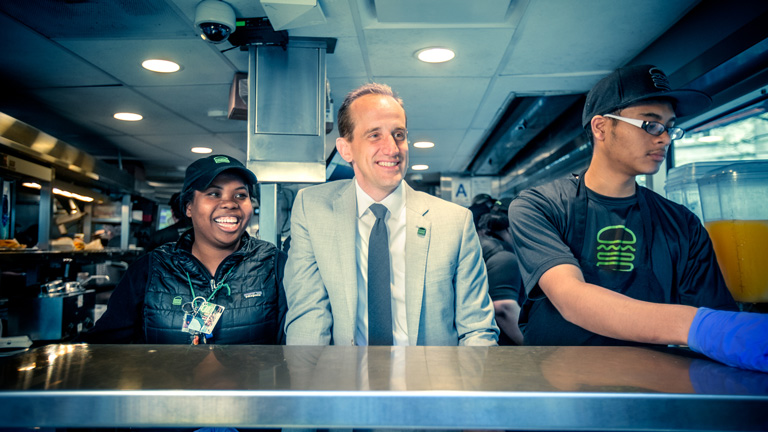 Randy Garutti stands behind the Shake Shack counter with two employees